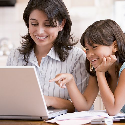 Woman and young girl in kitchen with laptop and paperwork smiling