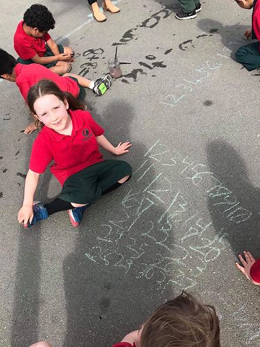 Sofia using chalk to write her numbers. Others using a paintbrush and water to make their numbers.