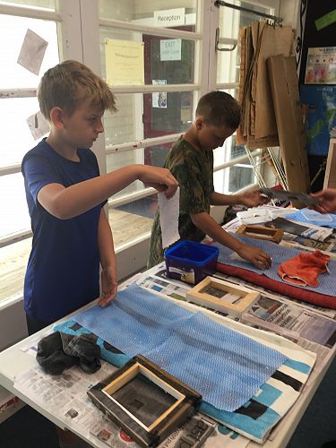 Jake and Cassius are peeling off the moist paper that they have just made.