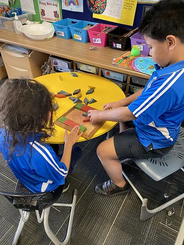 Tupuhi and Cyrus work together on a wooden shape puzzle.