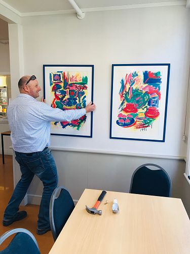 Mr Mick Geary hanging paintings by Marcia Scott (MacAuley) 
