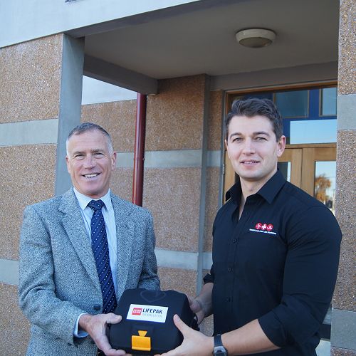 Mr Ross (left) receives the Automated External Defibrillator (AED) from Old Boy Craig Newton (2001-2005).