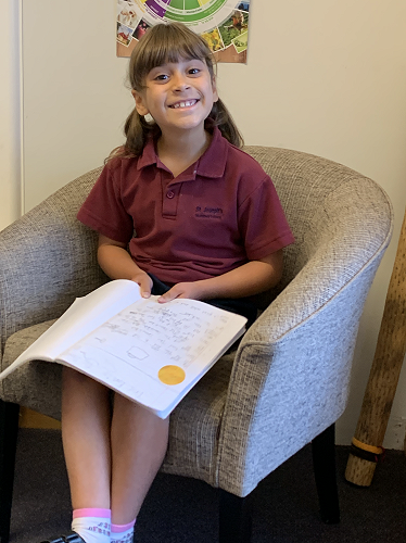 Sophia showing her principals certificate for writing an detailed retell of a story she read using the language